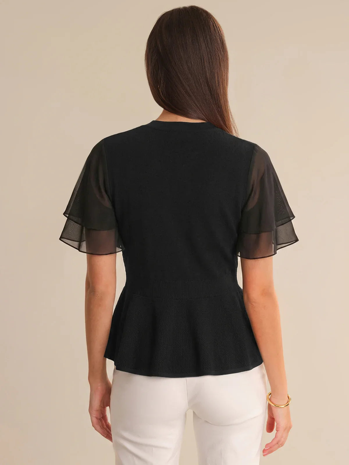 Woman wearing a black cardigan with sheer sleeves on a beige background