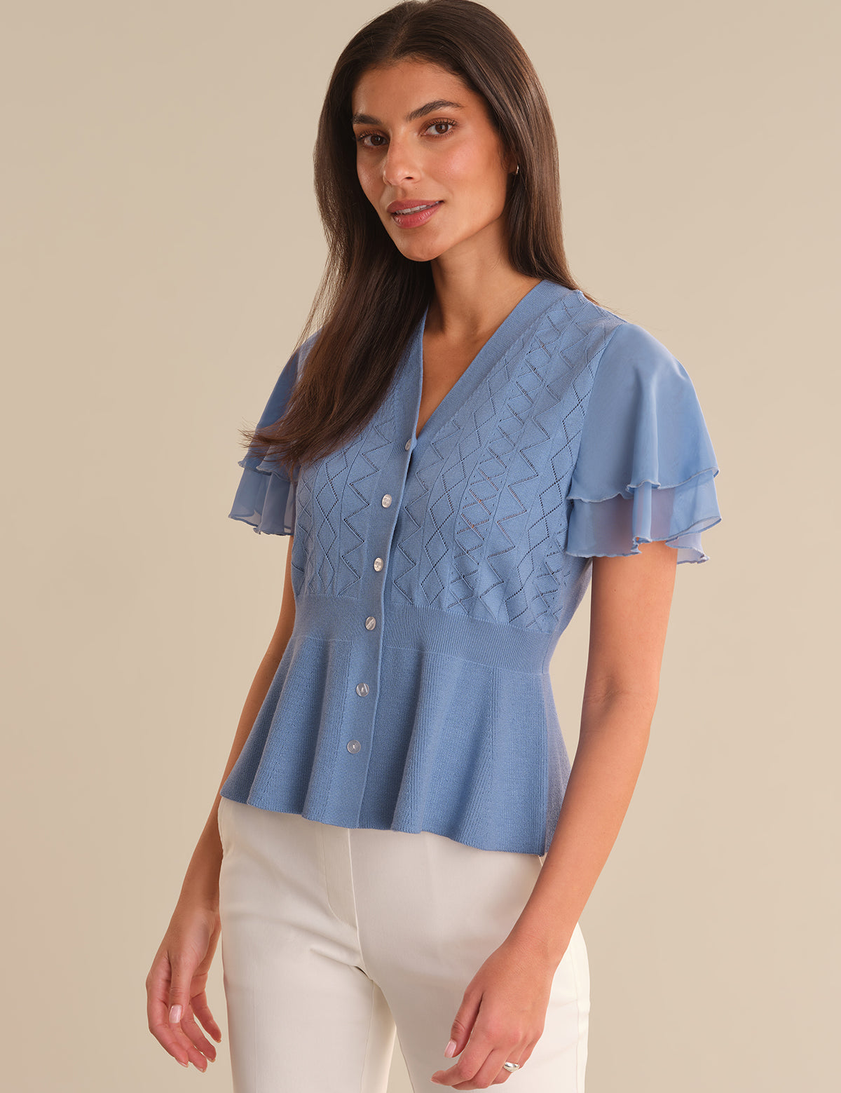 Woman wearing a blue cardigan with ruffled sleeves on a beige background