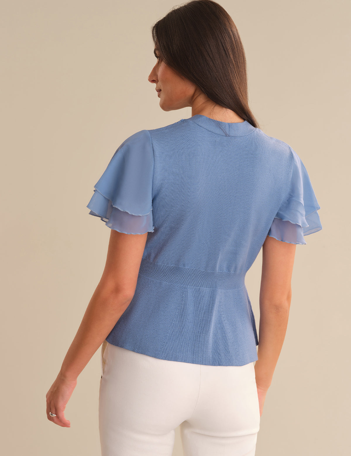 Woman wearing a blue cardigan with ruffled sleeves on a beige background