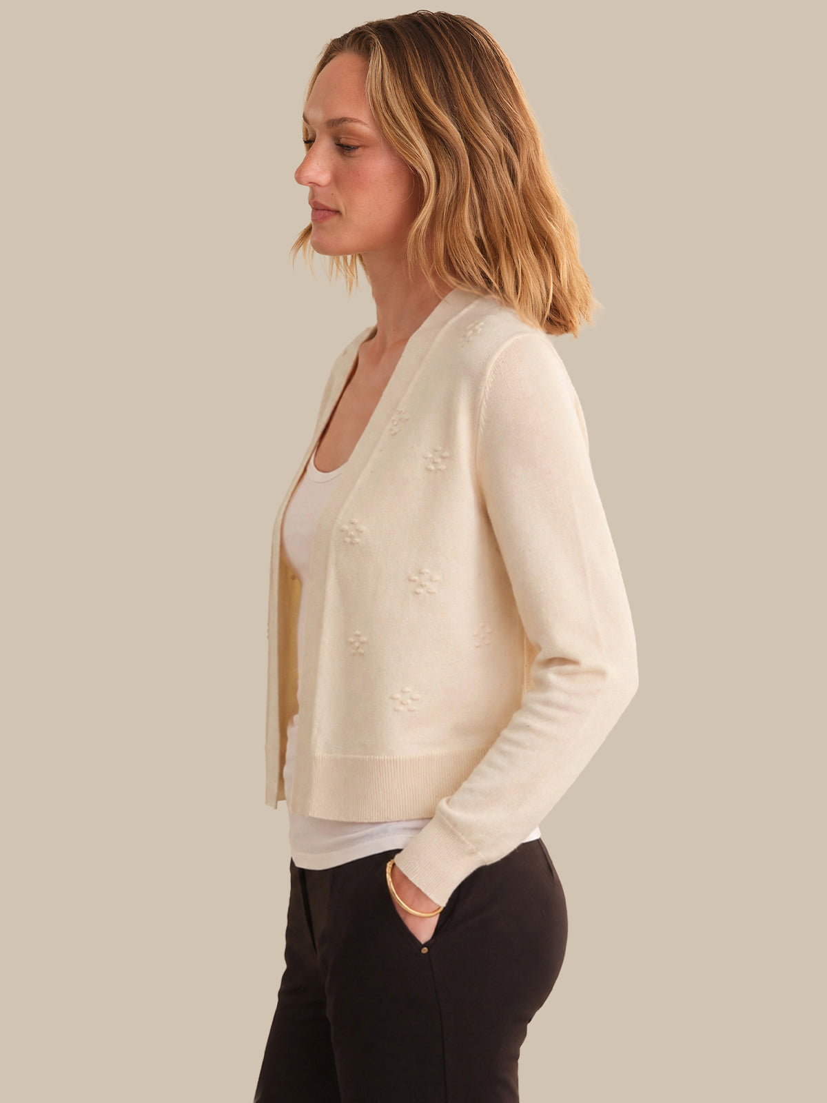 Woman wearing a cream cardigan over a white top and black pants on a neutral background