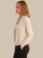 Woman wearing a cream cardigan over a white top and black pants on a neutral background