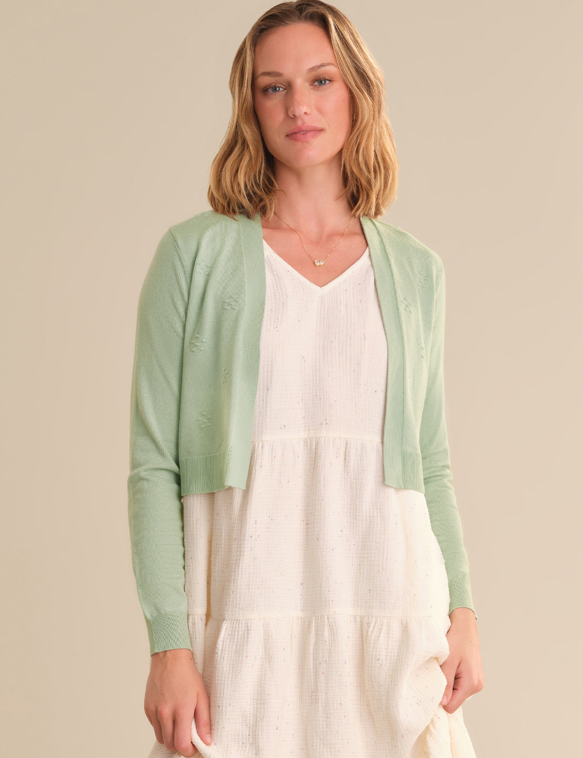 Woman wearing a light green cardigan over a white dress on a beige background