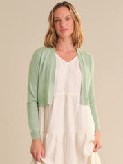 Woman wearing a light green cardigan over a white dress on a beige background