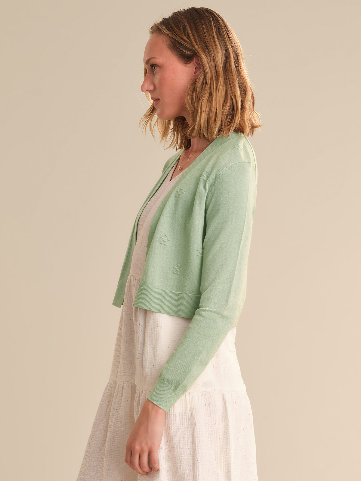 Woman wearing a light green cardigan over a white dress on a beige background