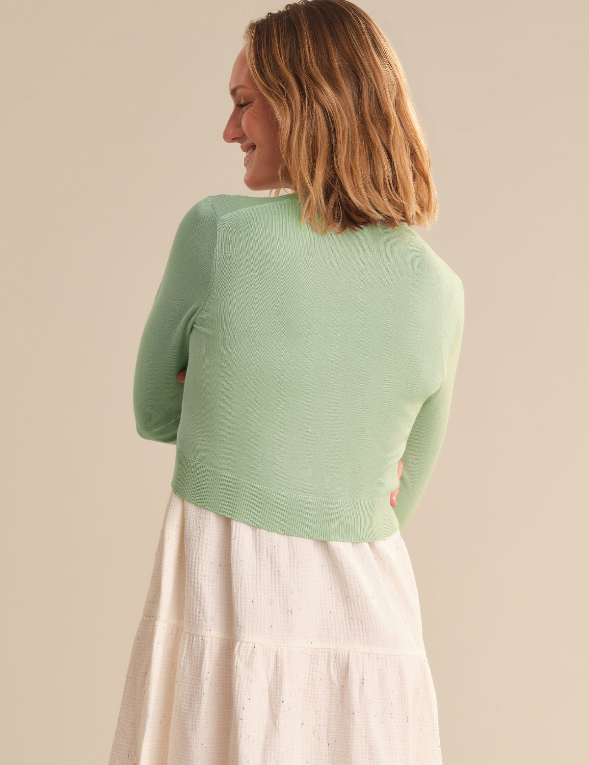 Woman wearing a light green sweater over a white skirt against a beige background