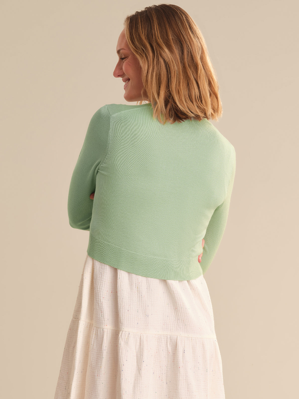 Woman wearing a light green sweater over a white skirt against a beige background