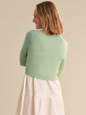 Woman wearing a light green sweater over a white skirt against a beige background