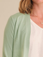 Person wearing a light green cardigan over a white top with a neutral background