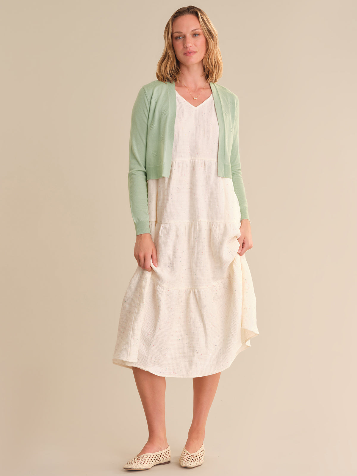 Woman wearing a white dress with a green cardigan on a beige background