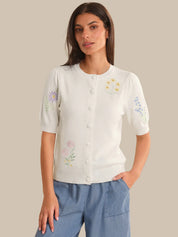 Woman wearing a white blouse with floral embroidery on a beige background