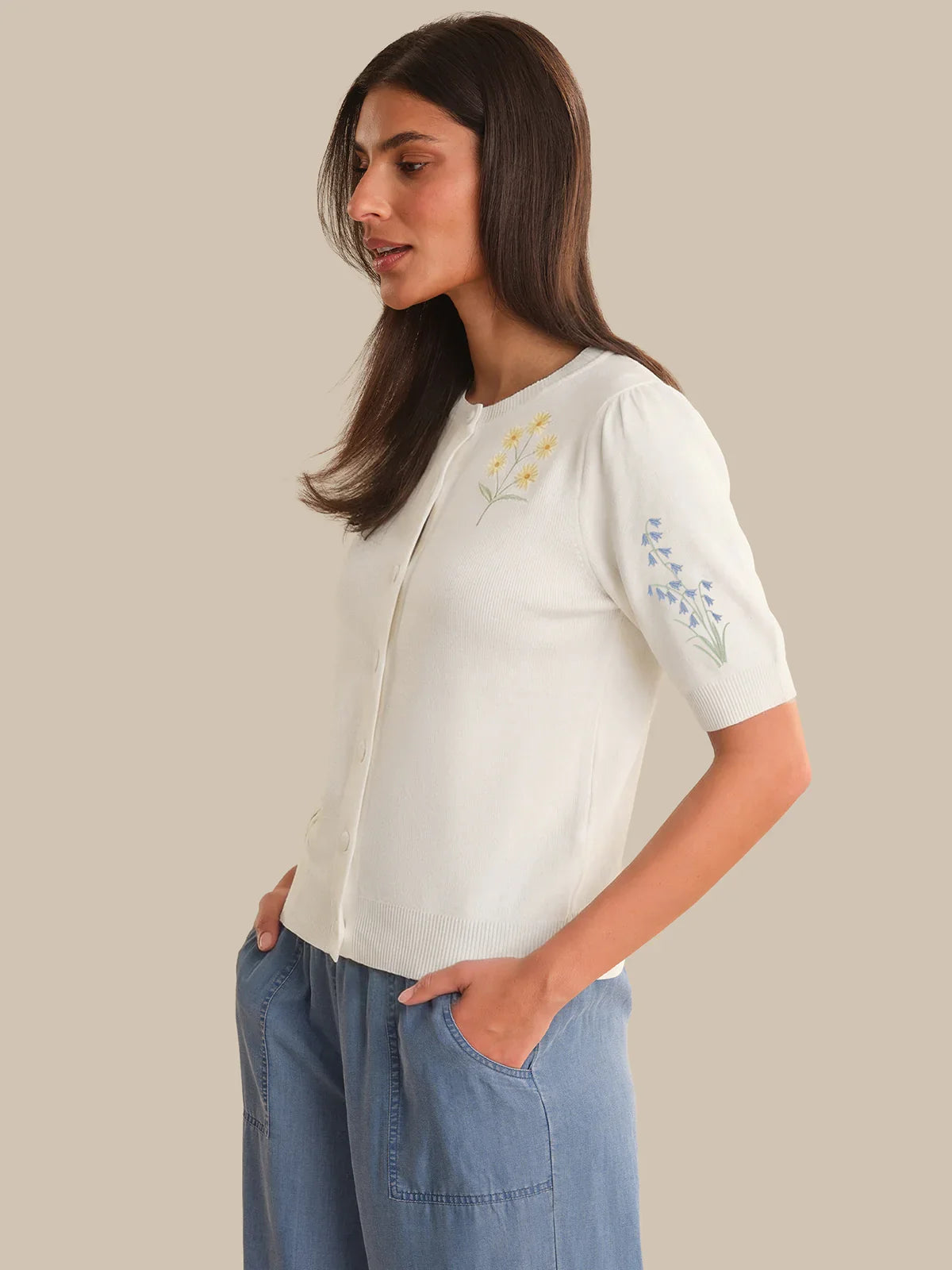 Woman wearing a white blouse with embroidery and blue pants on a beige background