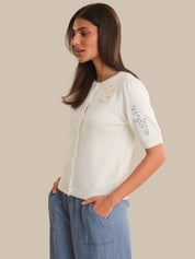Woman wearing a white blouse with embroidery and blue pants on a beige background