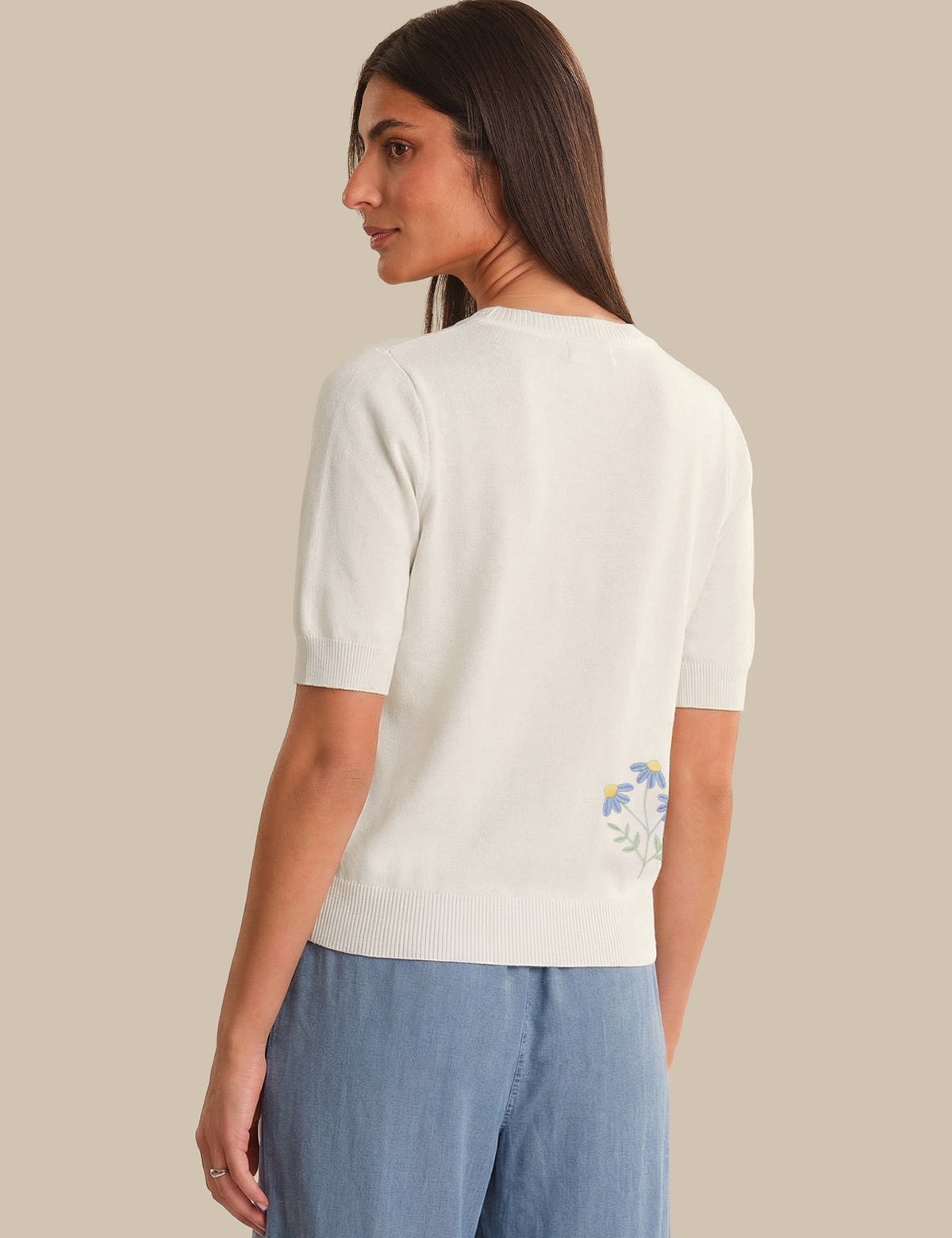 Woman wearing a white sweater with floral embroidery on a beige background