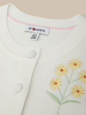 White cardigan with yellow floral embroidery and a visible brand tag on a beige background