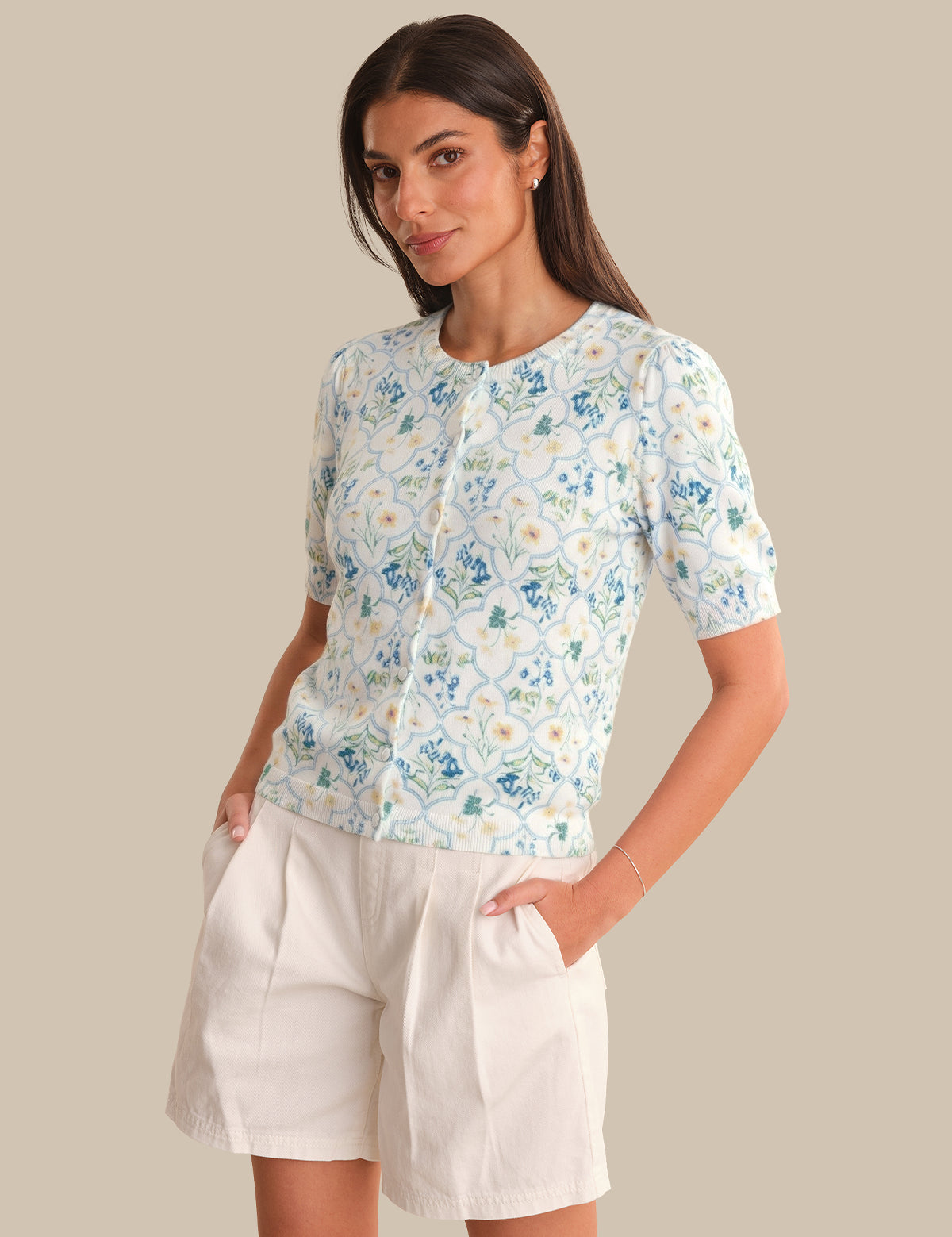 Woman wearing a floral cardigan and white shorts against a beige background