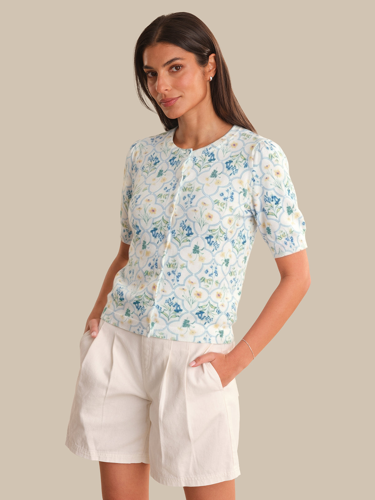 Woman wearing a floral cardigan and white shorts against a beige background