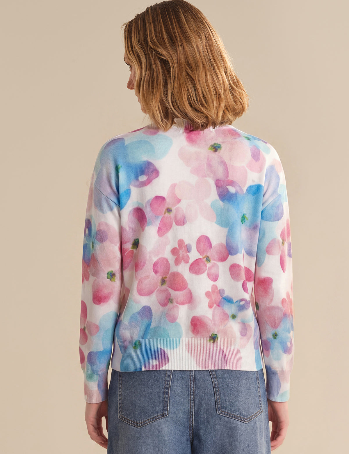 Person wearing a colorful floral cardigan against a beige background