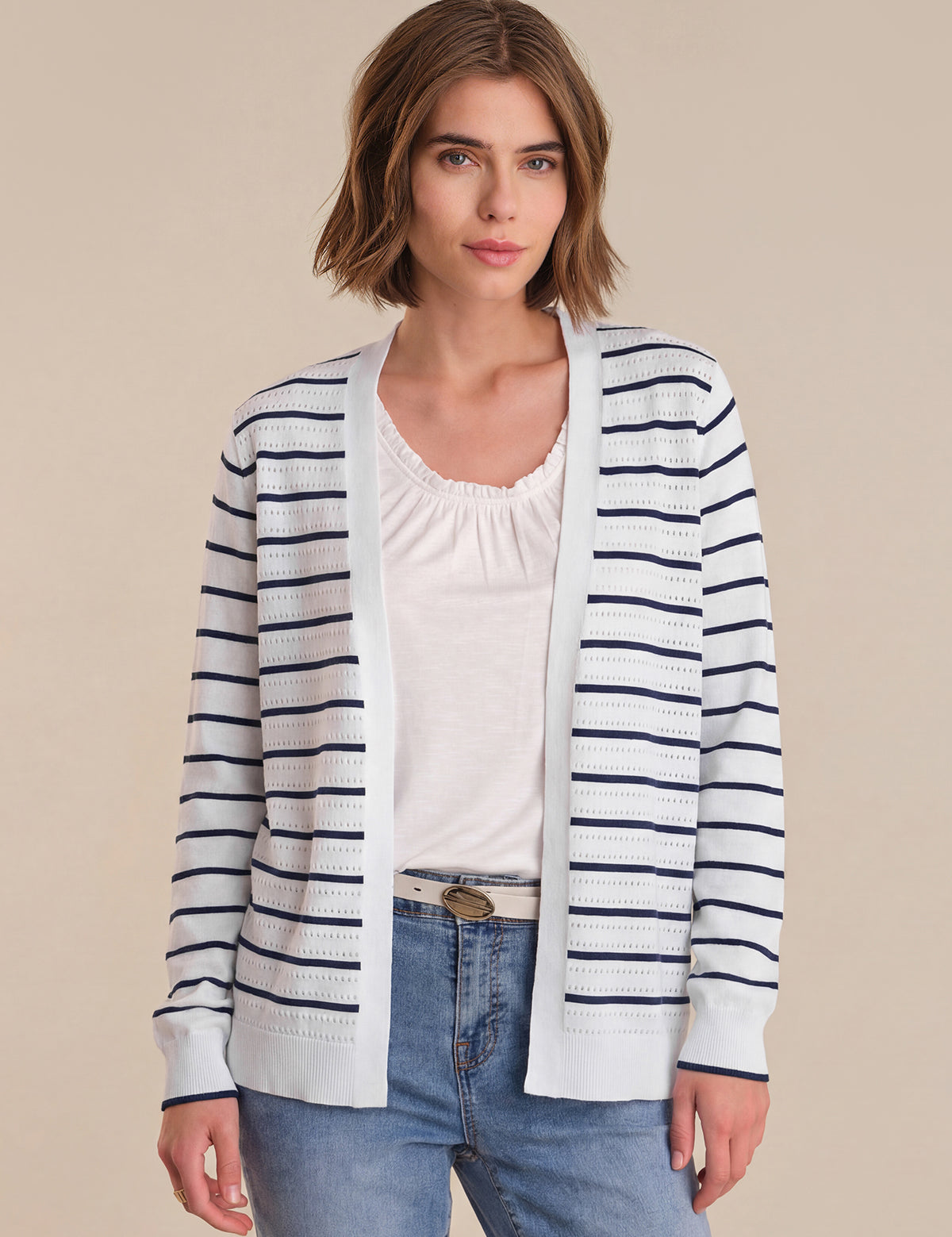 Woman wearing a striped cardigan over a white top and jeans on a beige background