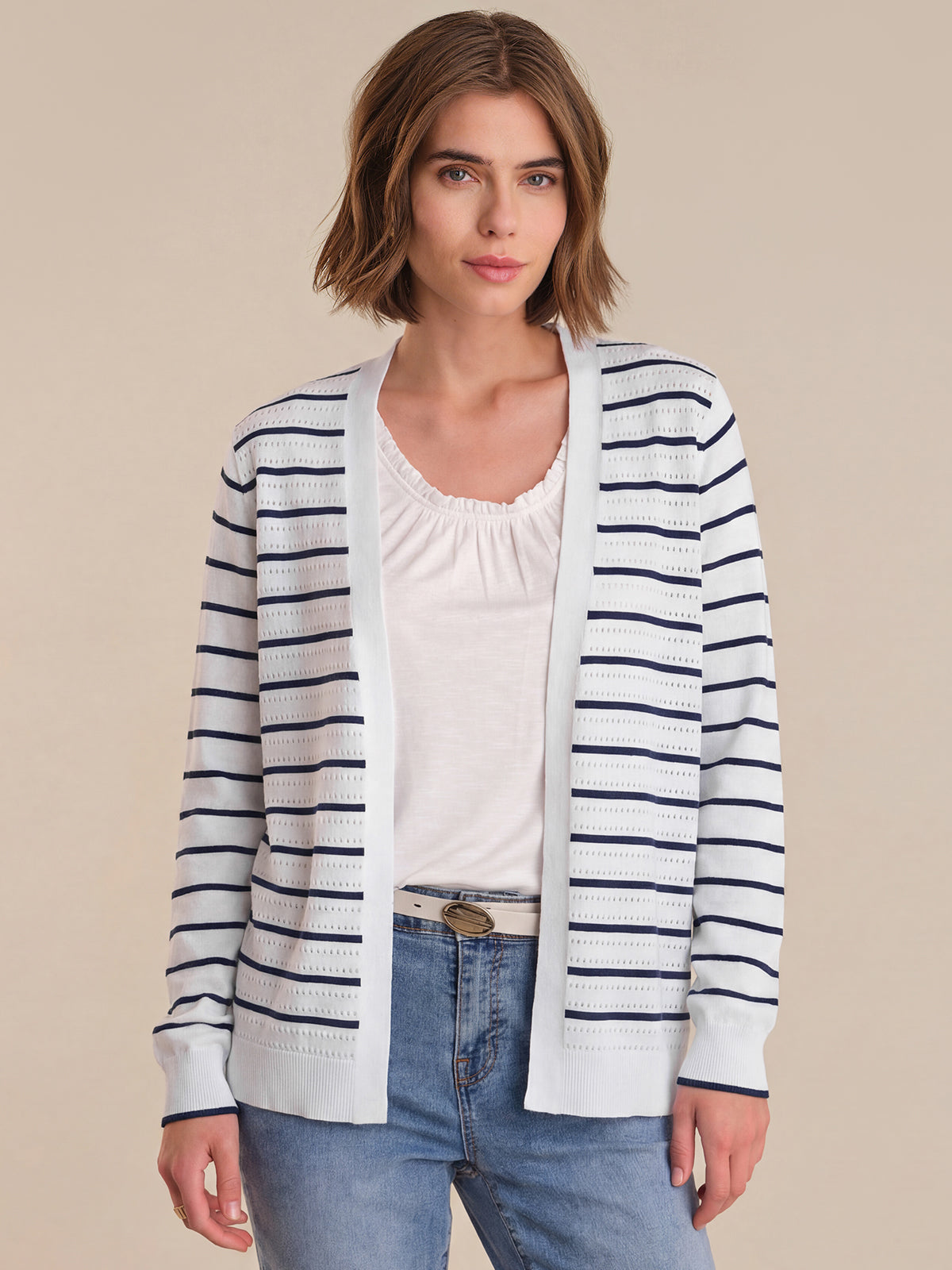 Woman wearing a striped cardigan over a white top and jeans on a beige background