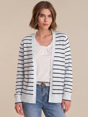 Woman wearing a striped cardigan over a white top and jeans on a beige background
