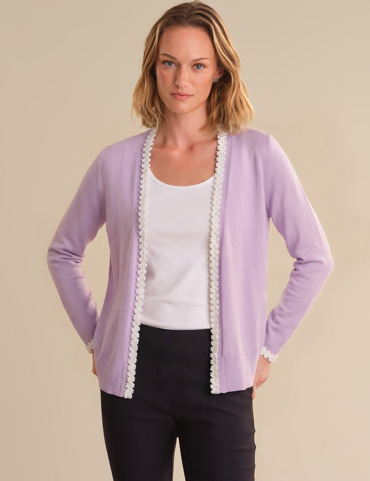Woman wearing a light purple cardigan with lace trim on a beige background