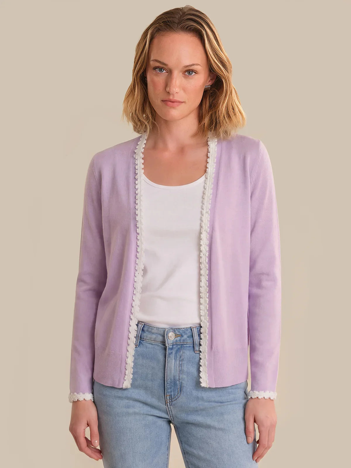 Woman wearing a light purple cardigan with lace trim over a white shirt and blue jeans on a beige background