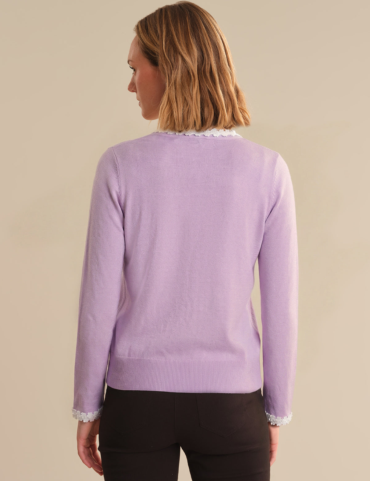 Woman wearing a purple sweater with lace trim on a beige background