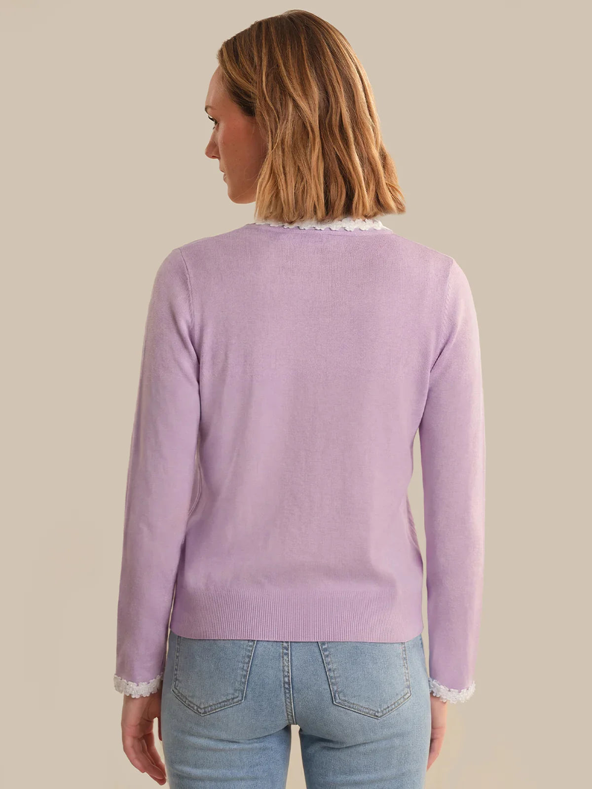 Woman wearing a light purple sweater with lace trim on a beige background
