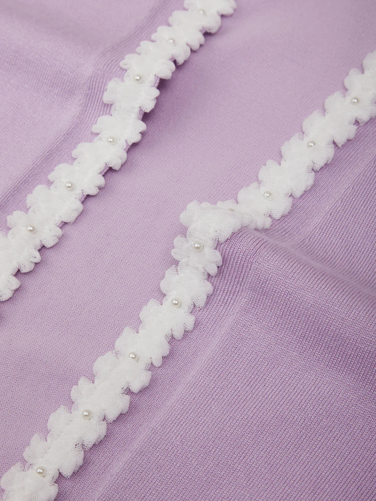 Close-up of white floral lace trim on a purple fabric background