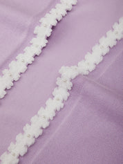 Close-up of white floral lace trim on a purple fabric background