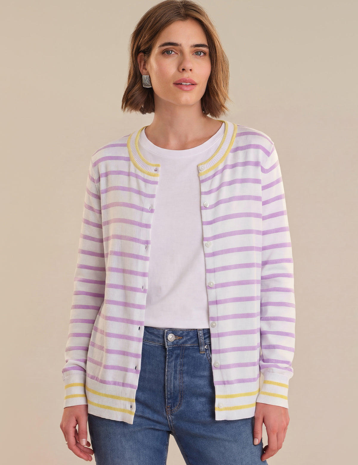 Woman wearing a striped cardigan over a white shirt with blue jeans on a beige background