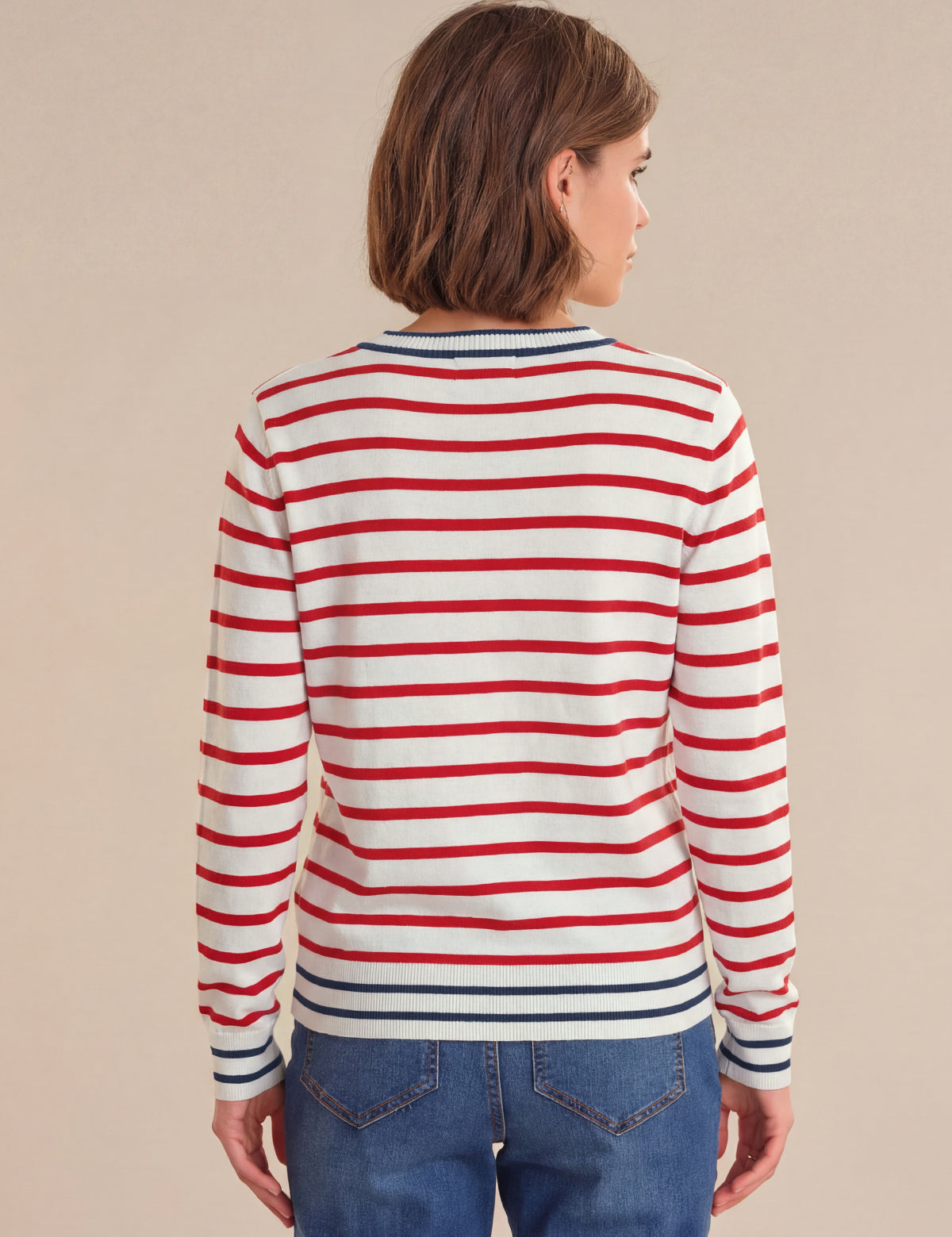 Person wearing a red and white striped long-sleeve shirt with blue jeans on a beige background