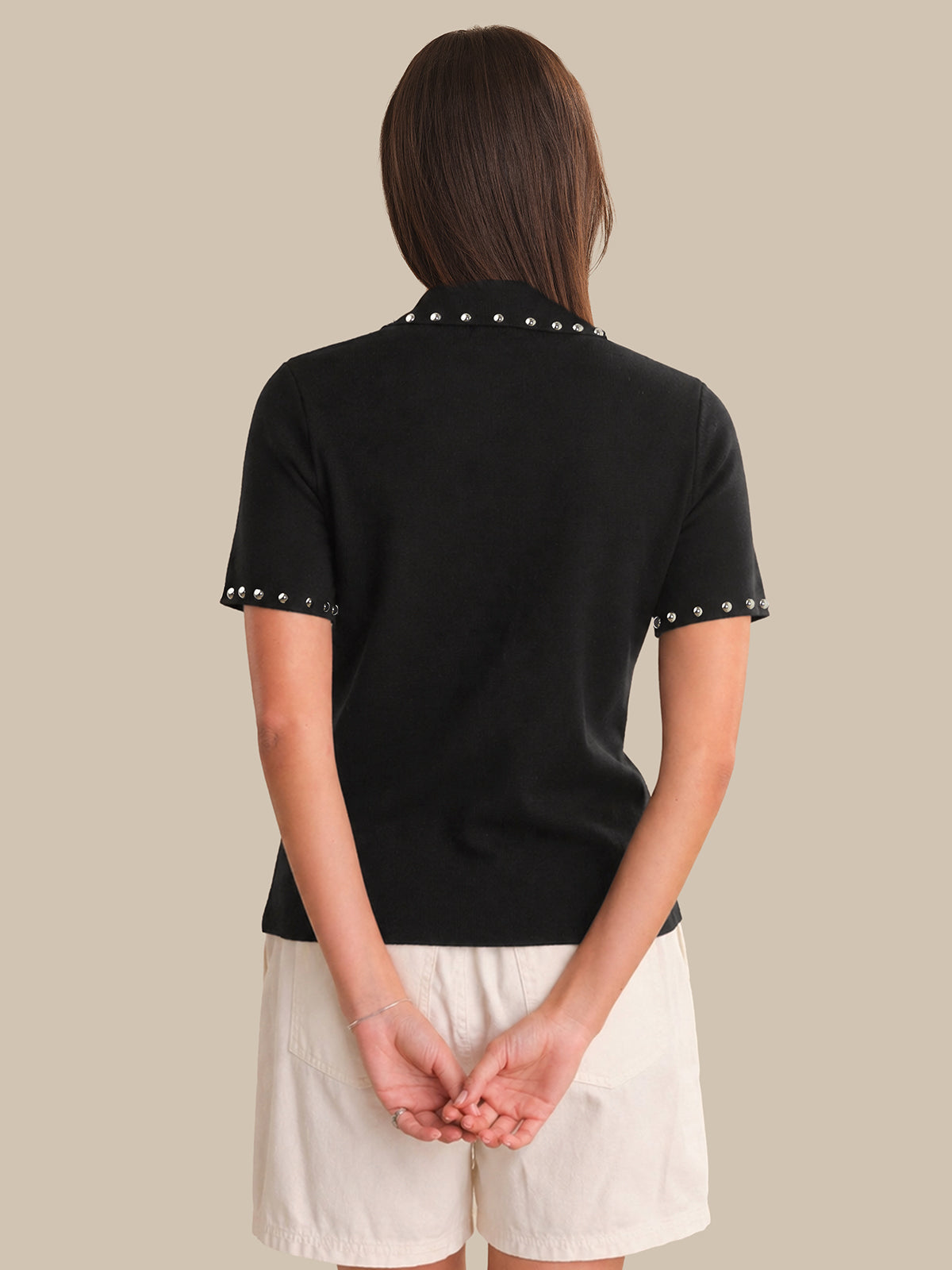 Person wearing a black polo shirt with decorative trim on a beige background