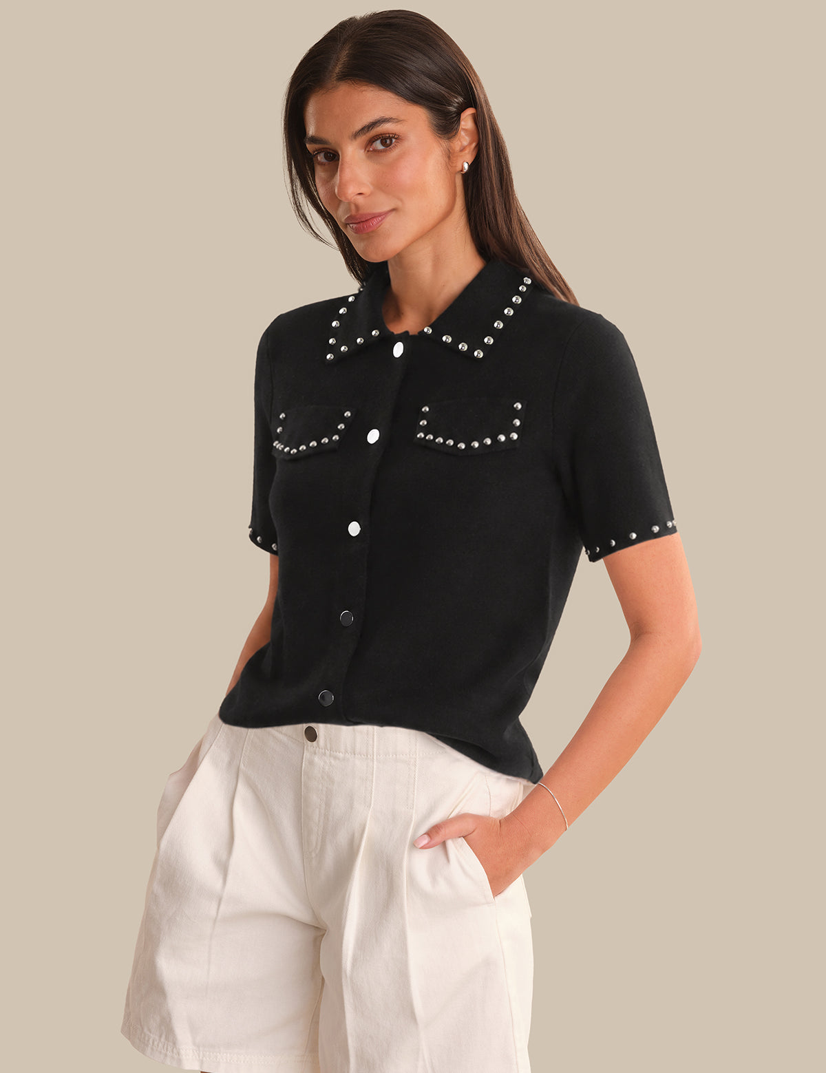 Woman wearing a black short-sleeve shirt with white buttons and trim, standing against a neutral background.