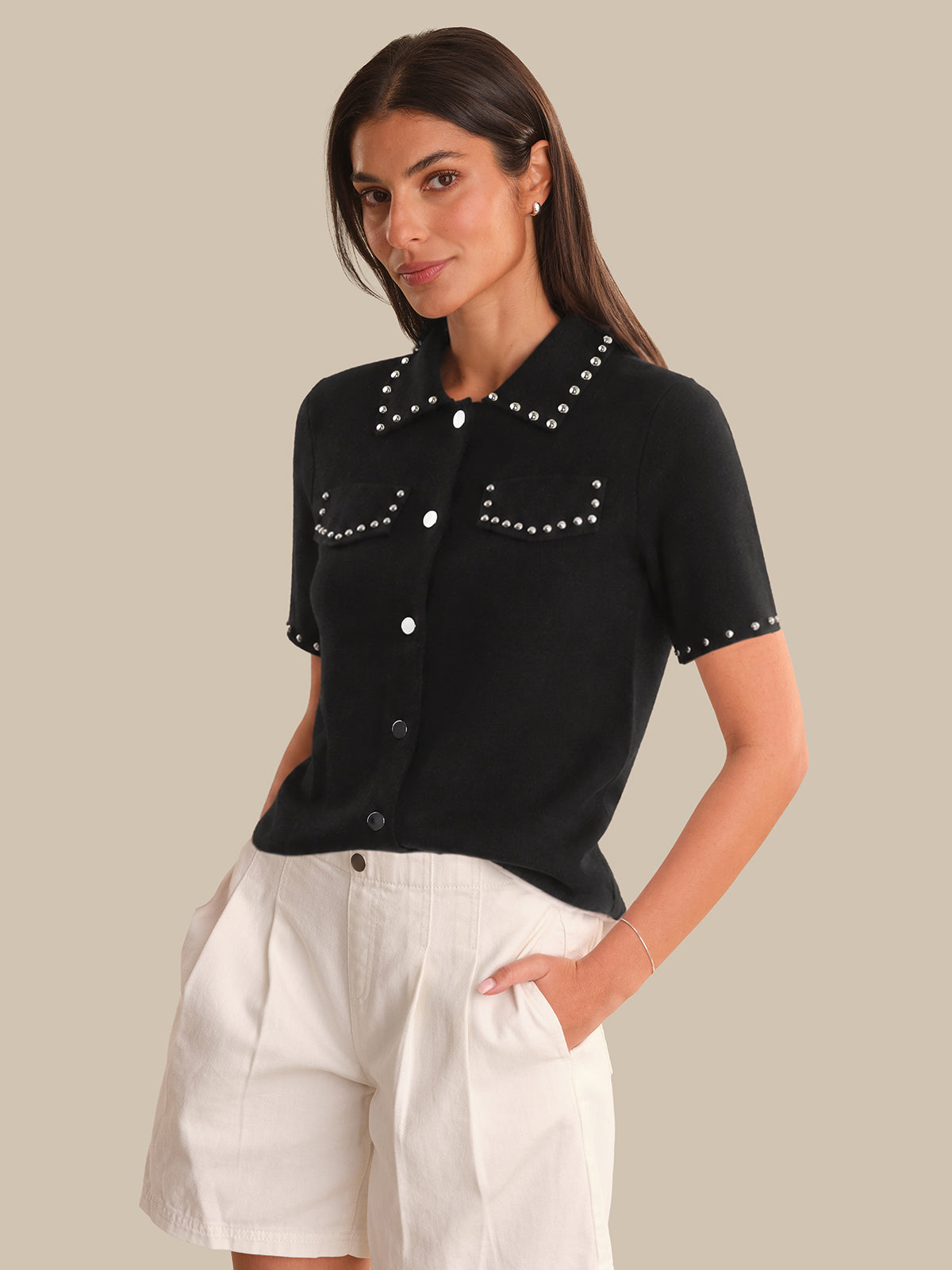 Woman wearing a black short-sleeve shirt with white buttons and trim, standing against a neutral background.