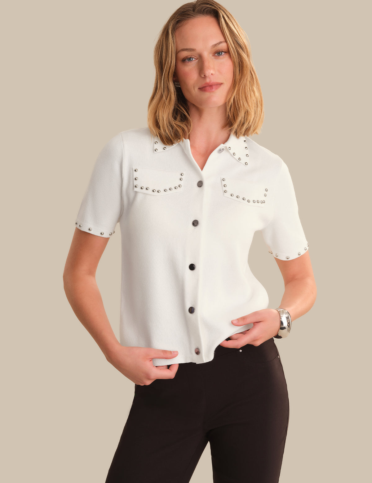 Woman wearing a white blouse with black buttons and embellishments on a beige background