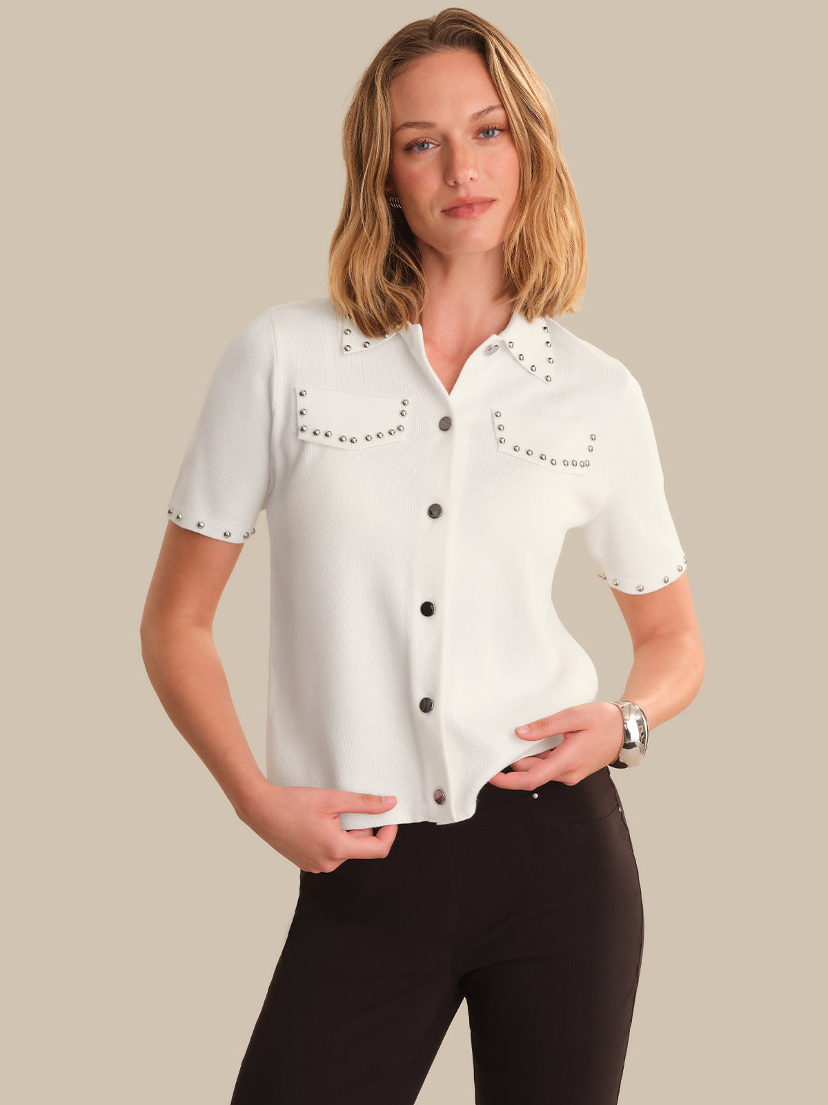 Woman wearing a white blouse with black buttons and embellishments on a beige background
