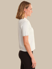 Woman wearing a white blouse with black pants against a plain background
