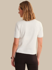Woman wearing a white short-sleeve shirt with black trim on a beige background