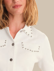 White blouse with studded details worn by a person, on a neutral background