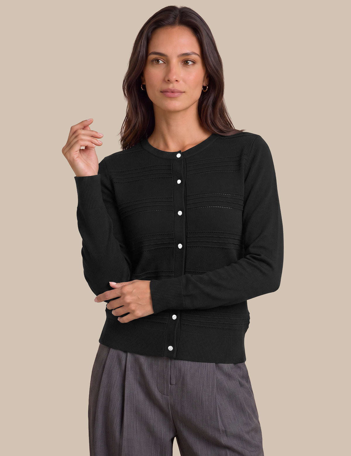 A woman modeling a black long-sleeve knit cardigan with a button-up front and horizontal ribbed texture, paired with gray trousers, against a solid beige background.