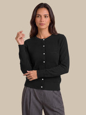 A woman modeling a black long-sleeve knit cardigan with a button-up front and horizontal ribbed texture, paired with gray trousers, against a solid beige background.