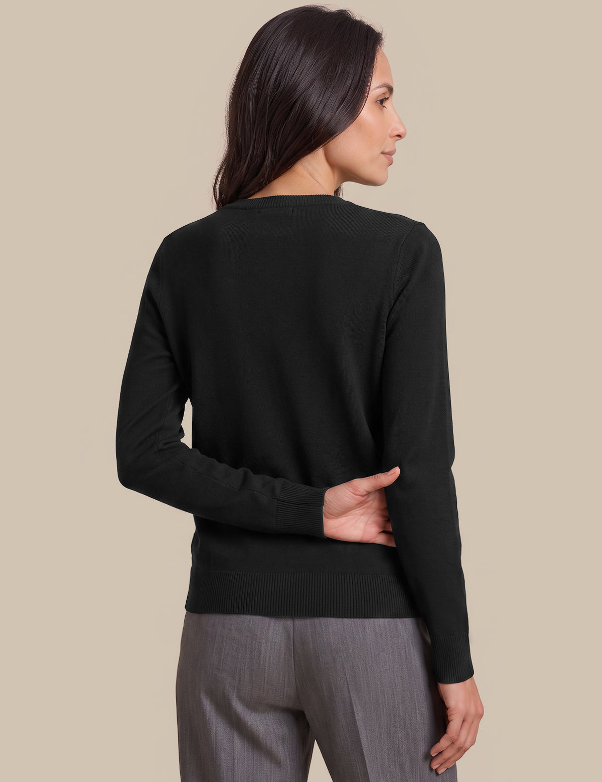 A woman shown from the back wearing a black long-sleeve knit sweater and gray trousers, standing against a solid beige studio background.