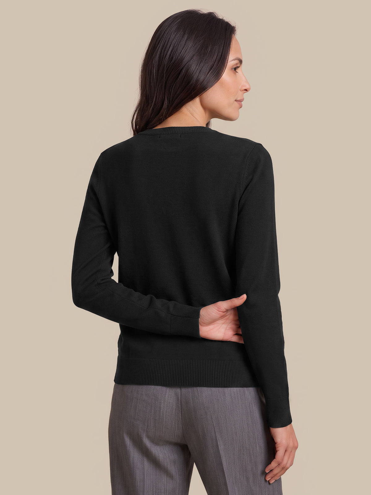 A woman shown from the back wearing a black long-sleeve knit sweater and gray trousers, standing against a solid beige studio background.
