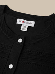 Close-up of a black ribbed knit cardigan sweater with a white button placket and a visible neck label reading 89th & Madison.