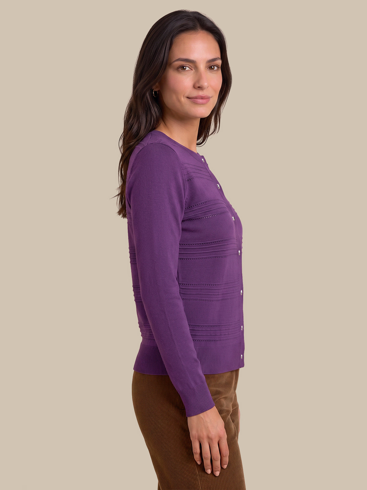 A woman shown in side profile wearing a purple long-sleeve button-front cardigan with horizontal ribbed details and brown pants, set against a solid beige background.
