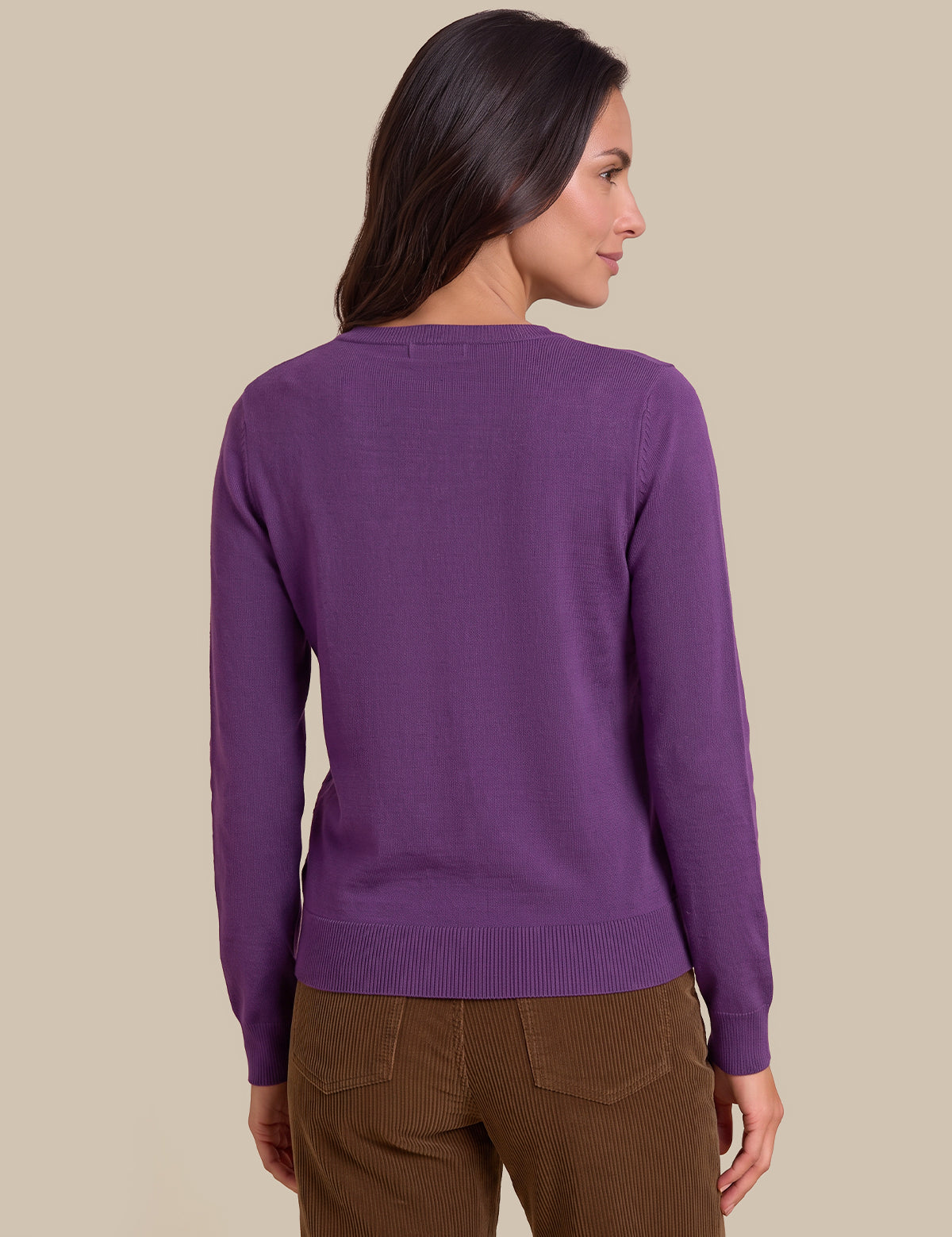 A woman shown from the back wearing a solid purple long-sleeve knit sweater and brown pants, set against a plain beige studio background.