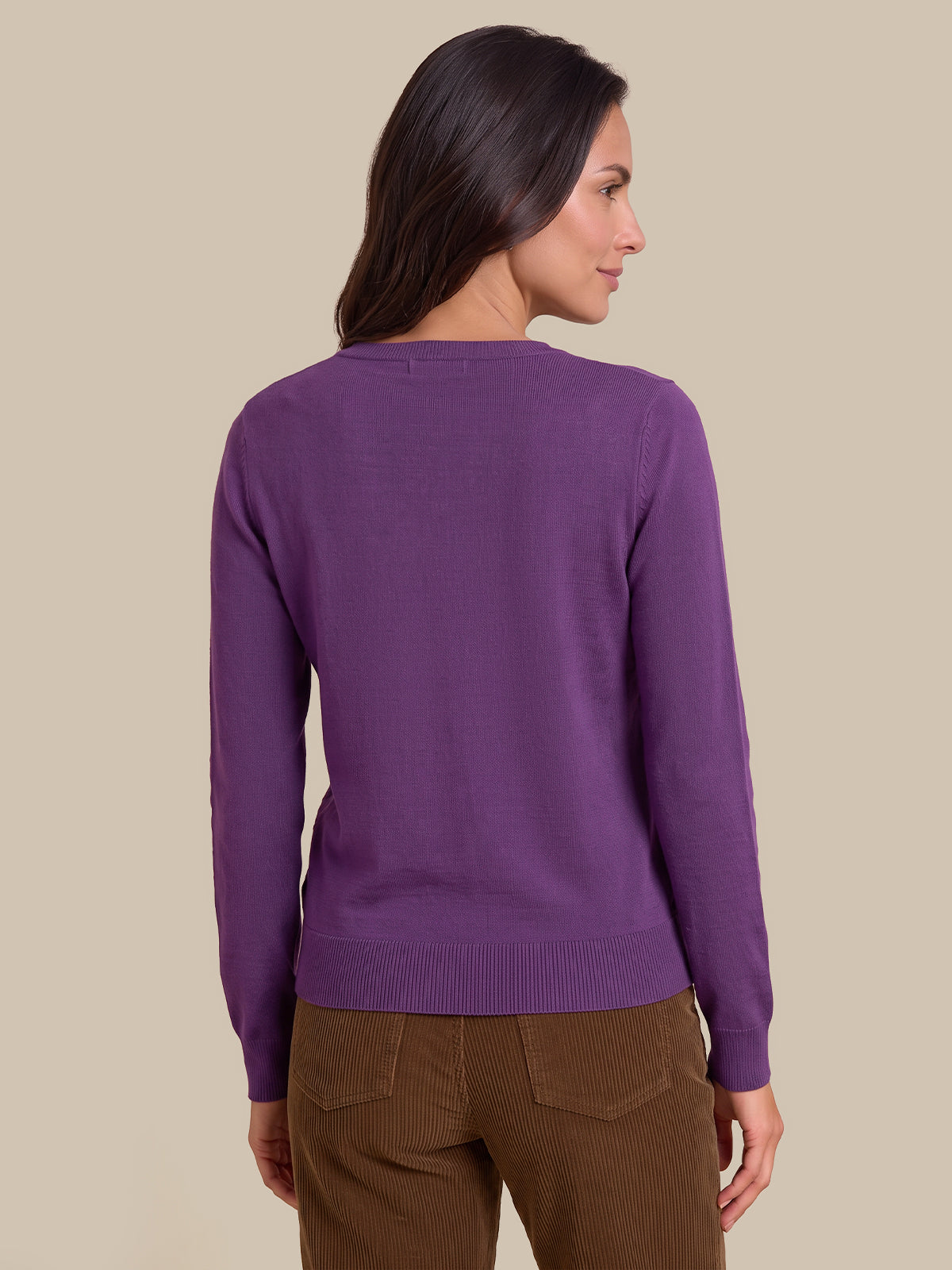 A woman shown from the back wearing a solid purple long-sleeve knit sweater and brown pants, set against a plain beige studio background.