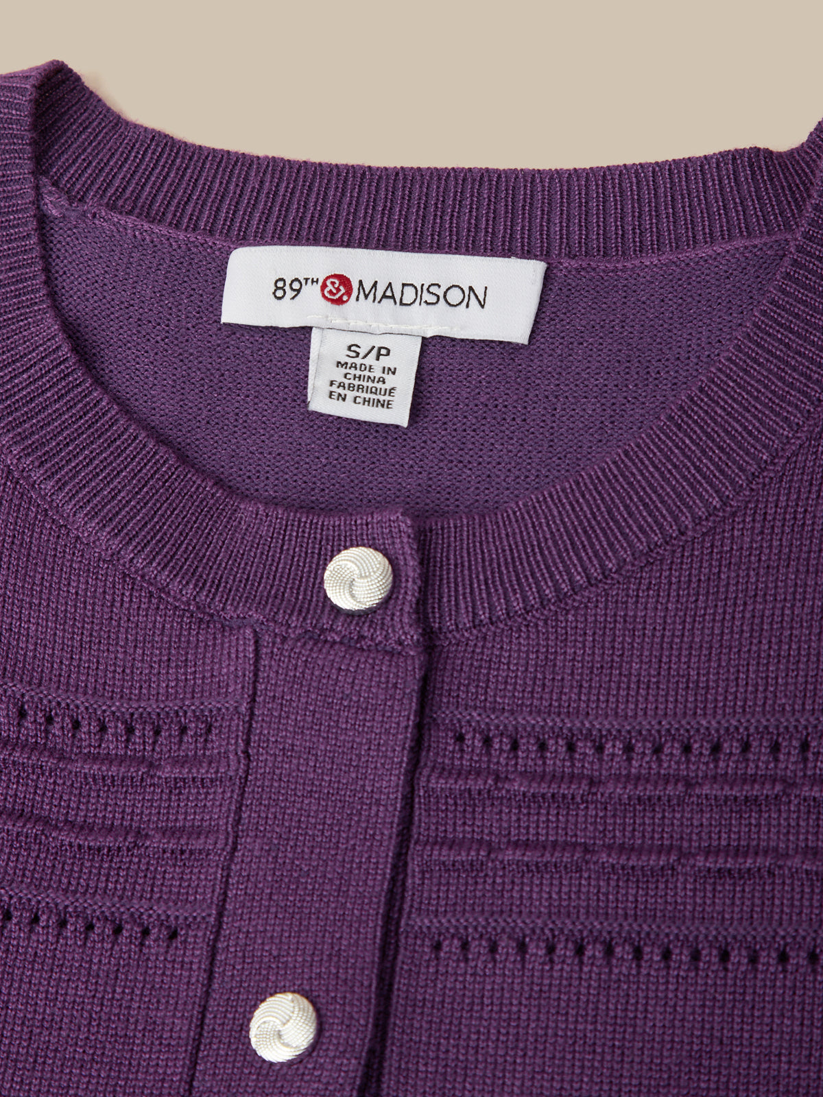 Close-up of a purple knit cardigan sweater with white buttons, showing the inside neck label that reads '89th Madison'.