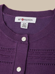 Close-up of a purple knit cardigan sweater with white buttons, showing the inside neck label that reads '89th Madison'.